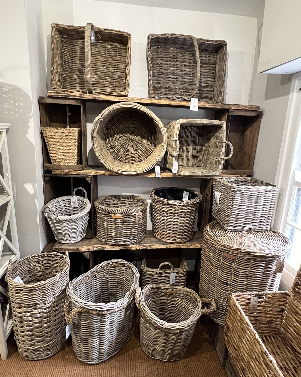 Wicker log baskets, trugs and shopping baskets stacked on dark wooden shelves