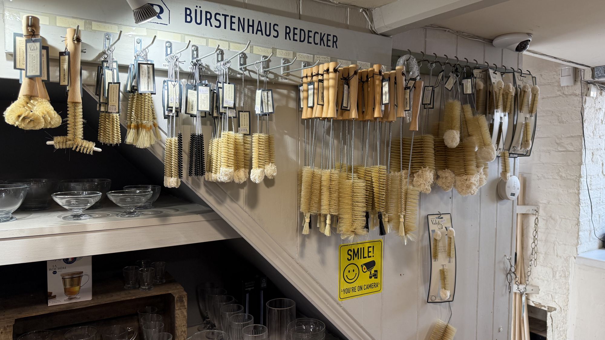 Wall of Bürstenhaus Redecker brushes hanging above shelves of glassware inside the shop